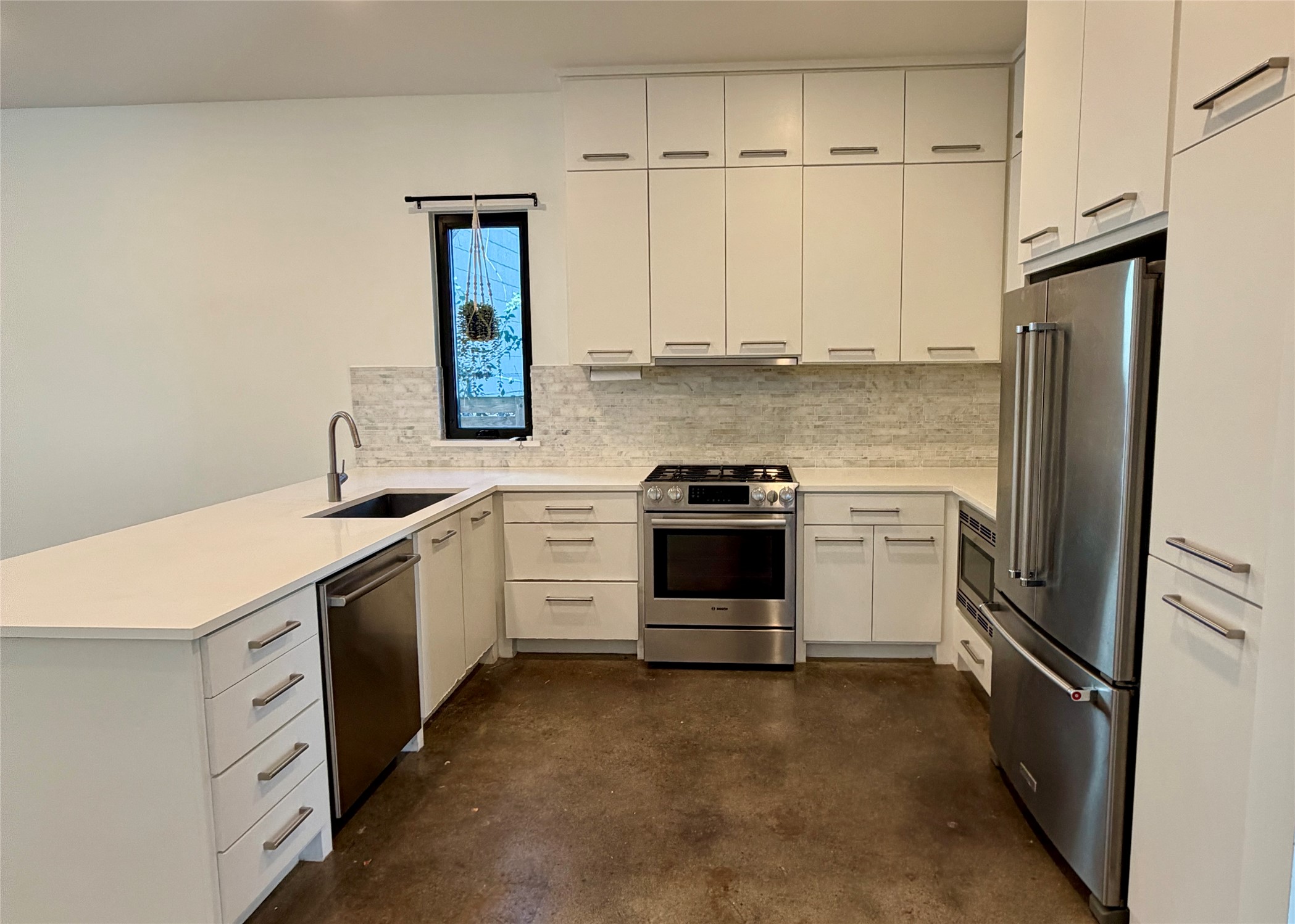 1515 Hether Street, Unit B Austin, TX 78704 - Photo 3 of 30 A contemporary kitchen features bright white cabinetry and stainless steel appliances, grounded by rich concrete flooring.