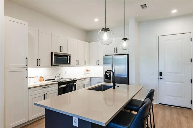 a kitchen with stainless steel appliances kitchen island granite countertop a sink a stove a refrigerator and white cabinets with wooden floor