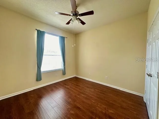 an empty room with wooden floor fan and windows