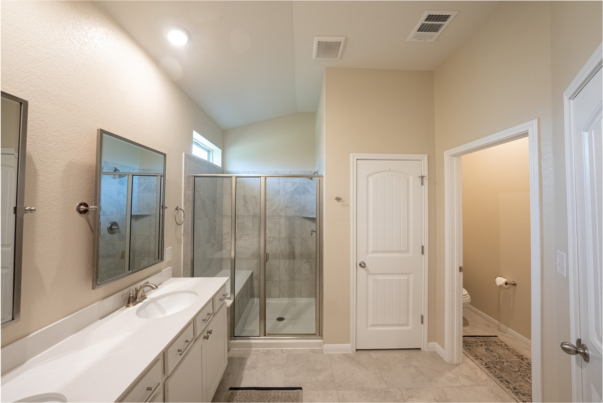 2508 Hat Bender Loop Round Rock, TX 78664 - Photo 13 of 22 Bathroom featuring a spacious double vanity with white countertops, a walk-in shower with glass enclosure, a private commode area, and sloped ceiling with a high window