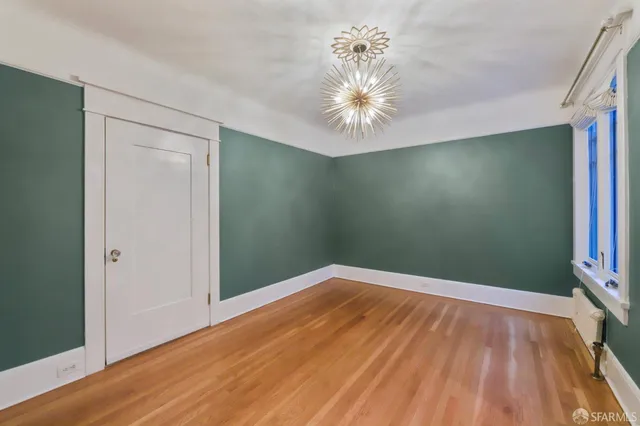 an empty room with wooden floor chandelier fan and windows