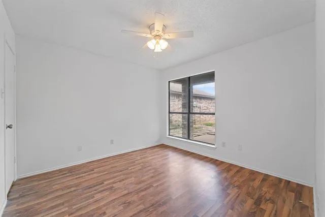 an empty room with wooden floor chandelier fan and windows