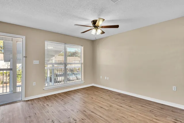 an empty room with wooden floor fan and windows