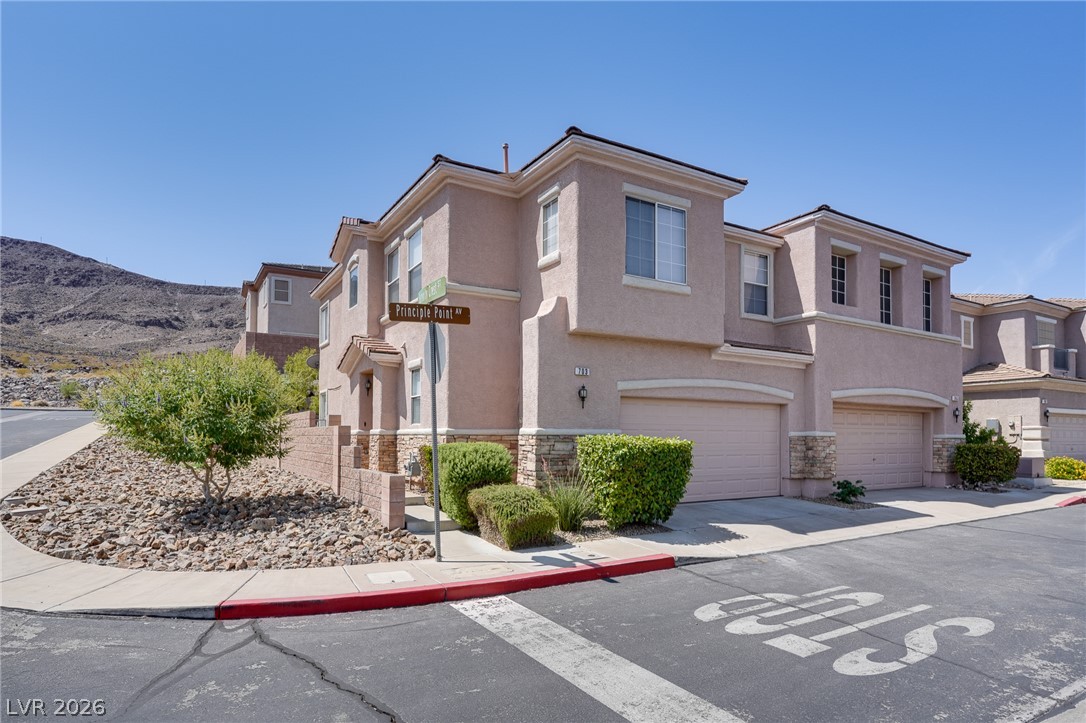703 Principle Point Avenue Henderson, NV 89012 - Photo 1 of 29 Multi-level dwellings with attached garages present a modern facade against a backdrop of arid hills.