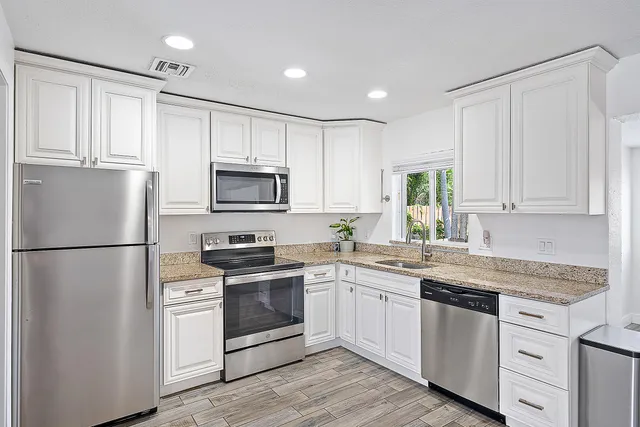 a kitchen with white cabinets white stainless steel appliances and sink