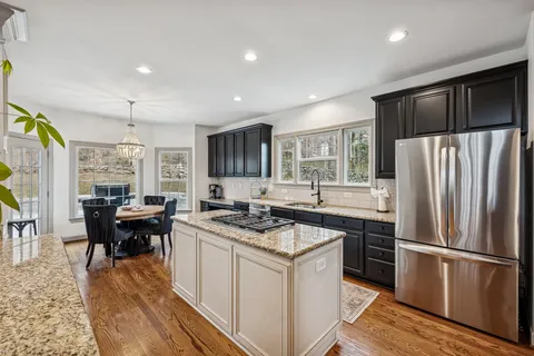 a kitchen with stainless steel appliances granite countertop a refrigerator a stove a sink dishwasher and a dining table with wooden floor
