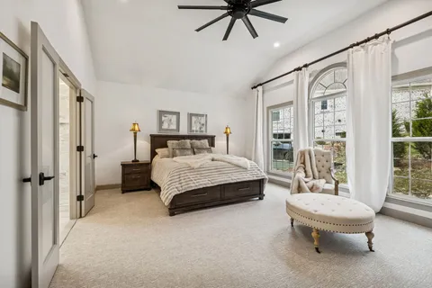 a spacious bedroom with a bed a chandelier and a glass walk in closet
