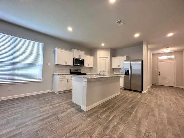 a large white kitchen with stainless steel appliances granite countertop a stove a sink a refrigerator white cabinets and wooden floor