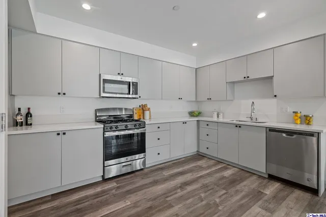 a kitchen with a stove a sink and white cabinets with wooden floor