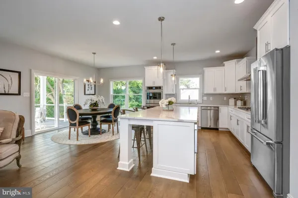 a kitchen with stainless steel appliances granite countertop a stove a refrigerator a kitchen island a dining table and chairs with wooden floor