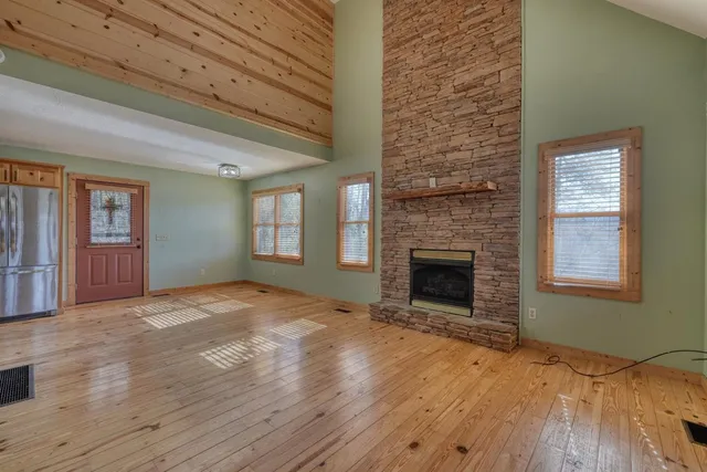 a view of an empty room with wooden floor fireplace and a window