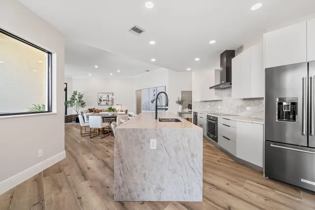 a large kitchen with stainless steel appliances kitchen island granite countertop a refrigerator a stove a sink a dining table and chairs with wooden floor