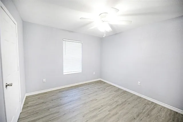 an empty room with wooden floor fan and window
