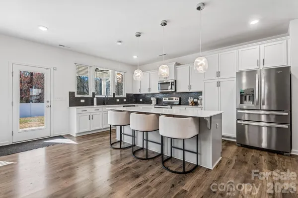 a kitchen with stainless steel appliances granite countertop a refrigerator a sink a stove and white cabinets with wooden floor