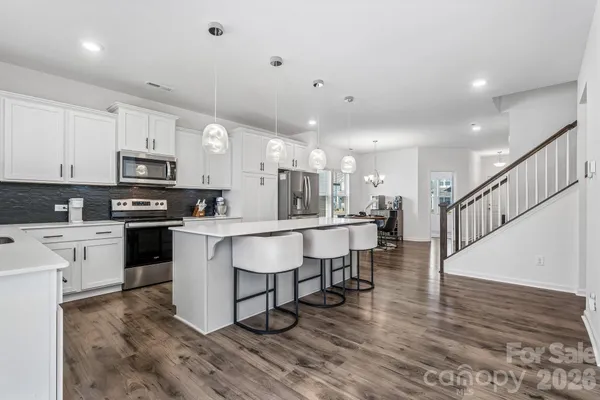 a kitchen with stainless steel appliances granite countertop a stove top oven a sink dishwasher a dining table and chairs with wooden floor