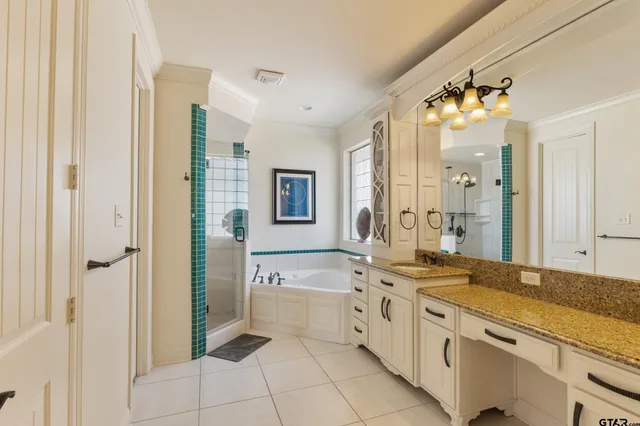 a spacious en suite bathroom with a granite countertop double vanity sink a mirror and a bathtub