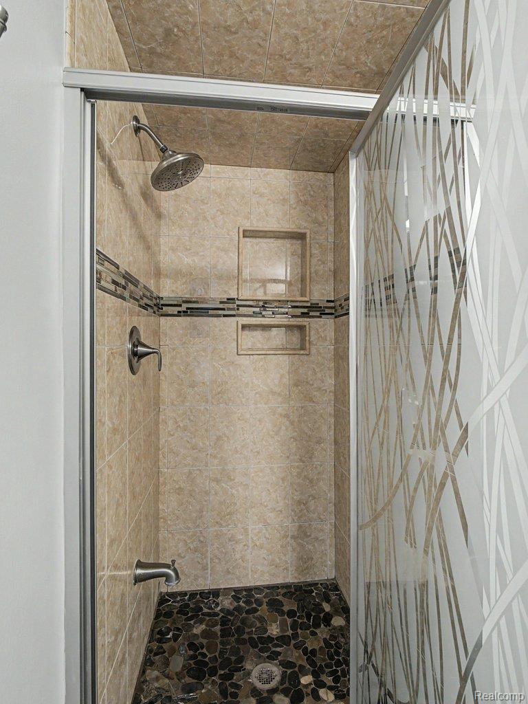 1974 Klingensmith Road, Unit 4 Bloomfield Hills, MI 48302 - Photo 17 of 35 Enclosed shower featuring earth-toned tile walls, multi-tone pebble flooring, and a decorative frosted glass shower door