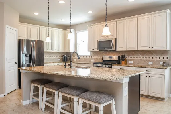 a kitchen with stainless steel appliances granite countertop a sink a stove a refrigerator cabinets and chairs