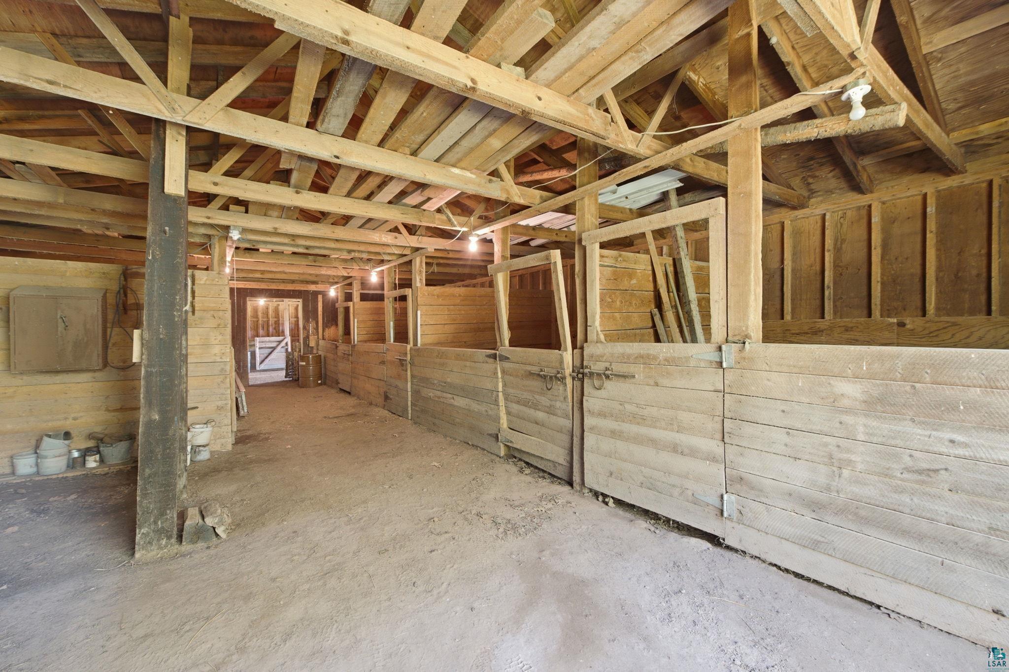 27485 South Kane Road Ashland, WI 54806 - Photo 19 of 35 Spacious barn interior featuring exposed wood beams and ceiling, multiple stalls with wood paneling, and an earthen floor