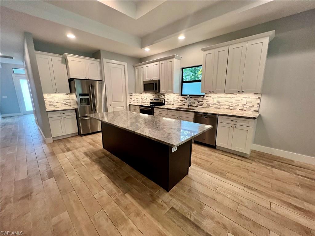 a large kitchen with kitchen island a sink dishwasher stove and white cabinets with wooden floor