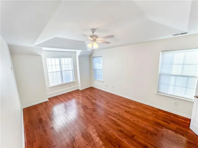 an empty room with wooden floor chandelier fan and windows