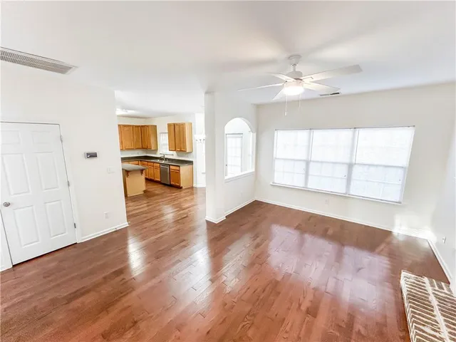 an empty room with wooden floor chandelier fan and windows