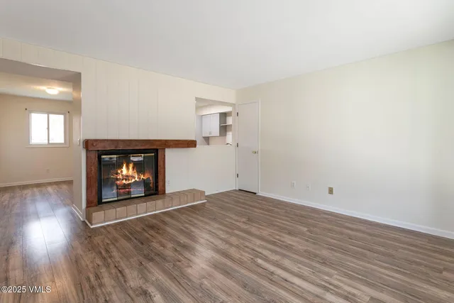 an empty room with wooden floor fire place and windows