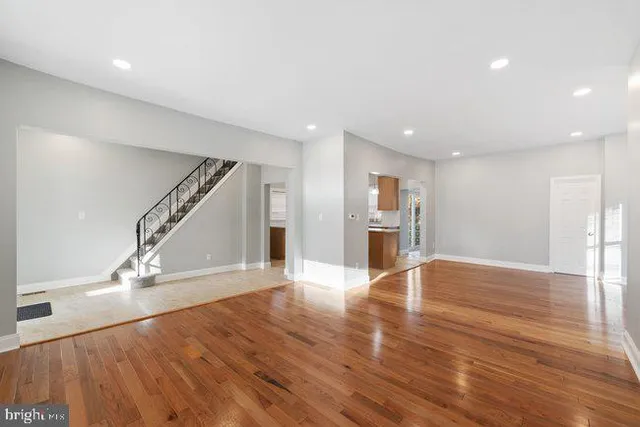 a view of an empty room with wooden floor kitchen view and a window