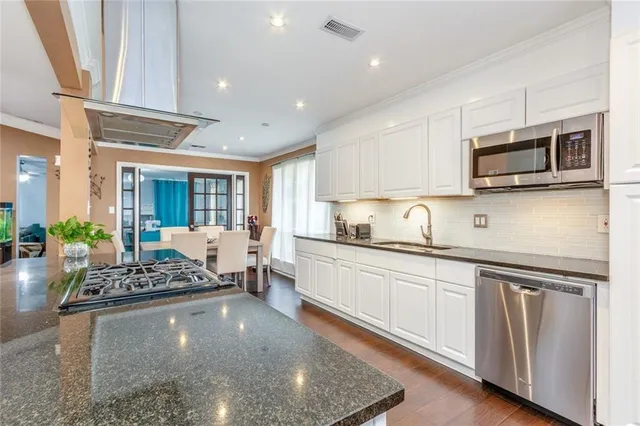 a kitchen with stainless steel appliances granite countertop a stove top oven a sink dishwasher a dining table and chairs with wooden floor