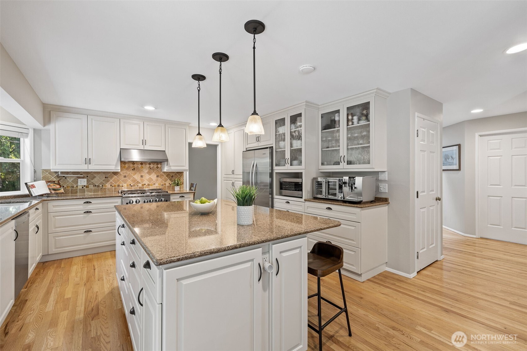4310 209th Avenue Northeast Sammamish, WA 98074 - Photo 11 of 39 a kitchen with stainless steel appliances kitchen island granite countertop a stove a sink and white cabinets with wooden floor