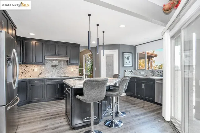 a kitchen with granite countertop kitchen island stainless steel appliances a dining table chairs sink and cabinets