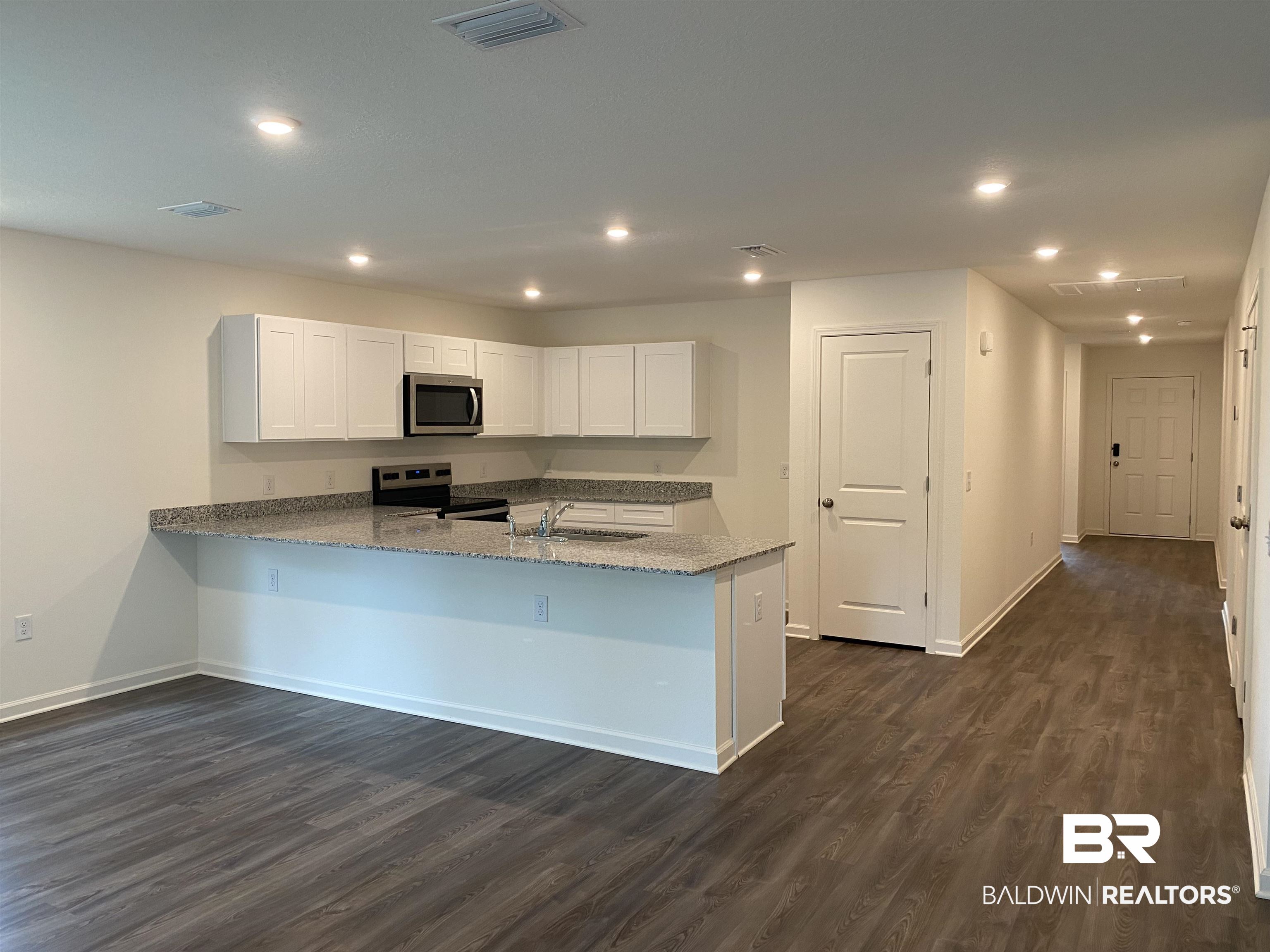 21676 Yosemite Boulevard Fairhope, AL 36532 - Photo 2 of 19 Kitchen featuring light stone counters, dark wood-type flooring, white cabinets, kitchen peninsula, and stainless steel appliances