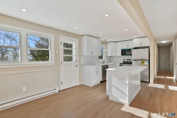a large white kitchen with stainless steel appliances granite countertop a refrigerator a stove a sink and white cabinets with wooden floor