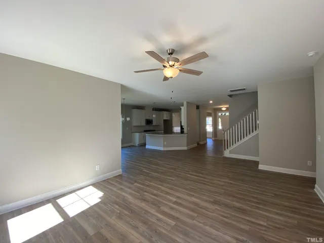 a view of an empty room with wooden floor and a ceiling fan