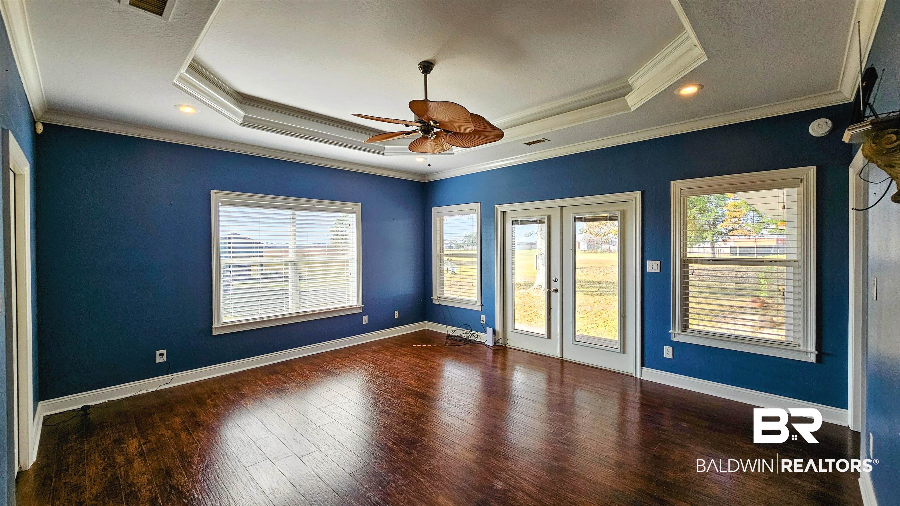 9275 Crawford Road Elberta, AL 36530 - Photo 13 of 28 Empty room with dark wood-style floors, a tray ceiling, french doors, a ceiling fan, and ornamental molding