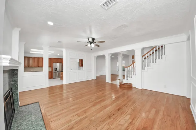 a view of an empty room with wooden floor and a kitchen