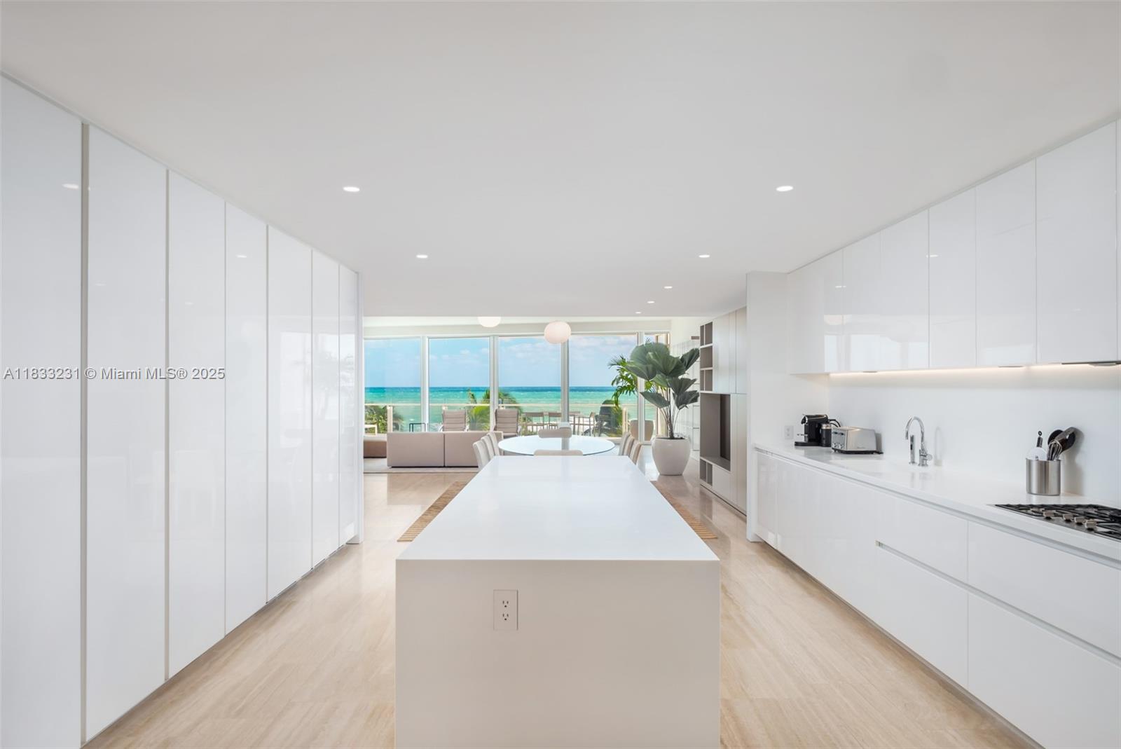 9001 Collins Avenue, Unit S305 Surfside, FL 33154 - Photo 13 of 23 a large white kitchen with kitchen island a large counter space a sink a stove and white cabinets