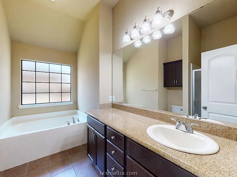 2024 Mountain Wind Loop Bryan, TX 77807 - Photo 8 of 14 a bathroom with a granite countertop sink a large mirror and a bathtub