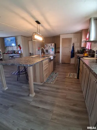 a kitchen with kitchen island granite countertop wooden floors and a view of living room