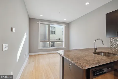 a view of an empty room with wooden floor and a kitchen