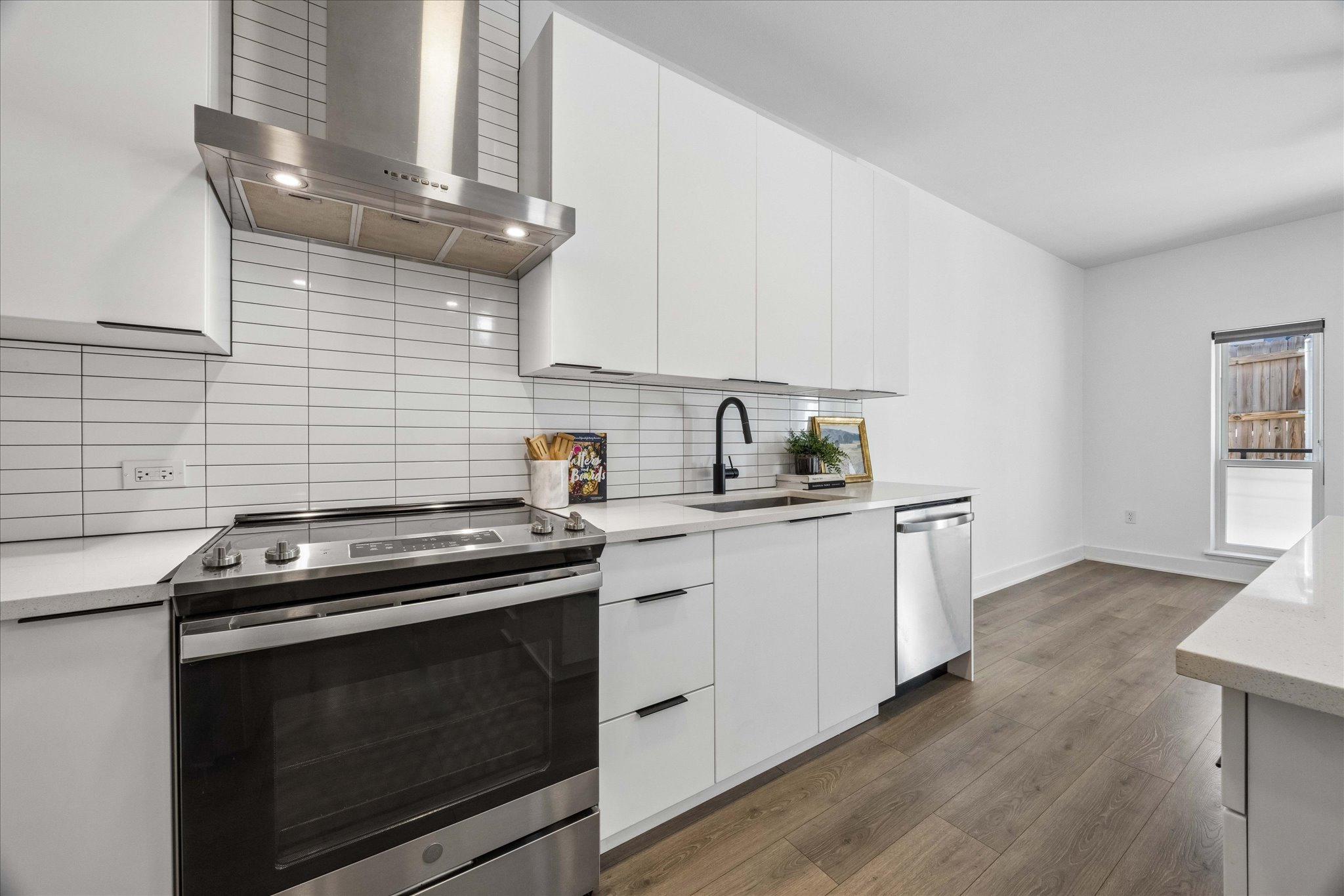 2220 Webberville Road, Unit 216 Austin, TX 78702 - Photo 7 of 26 Modern kitchen featuring white flat-panel cabinetry, stainless steel appliances, a subway tile backsplash, and wood-finish flooring