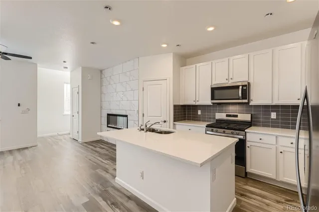 a kitchen with stainless steel appliances a stove top oven a sink a refrigerator white cabinets and wooden floor