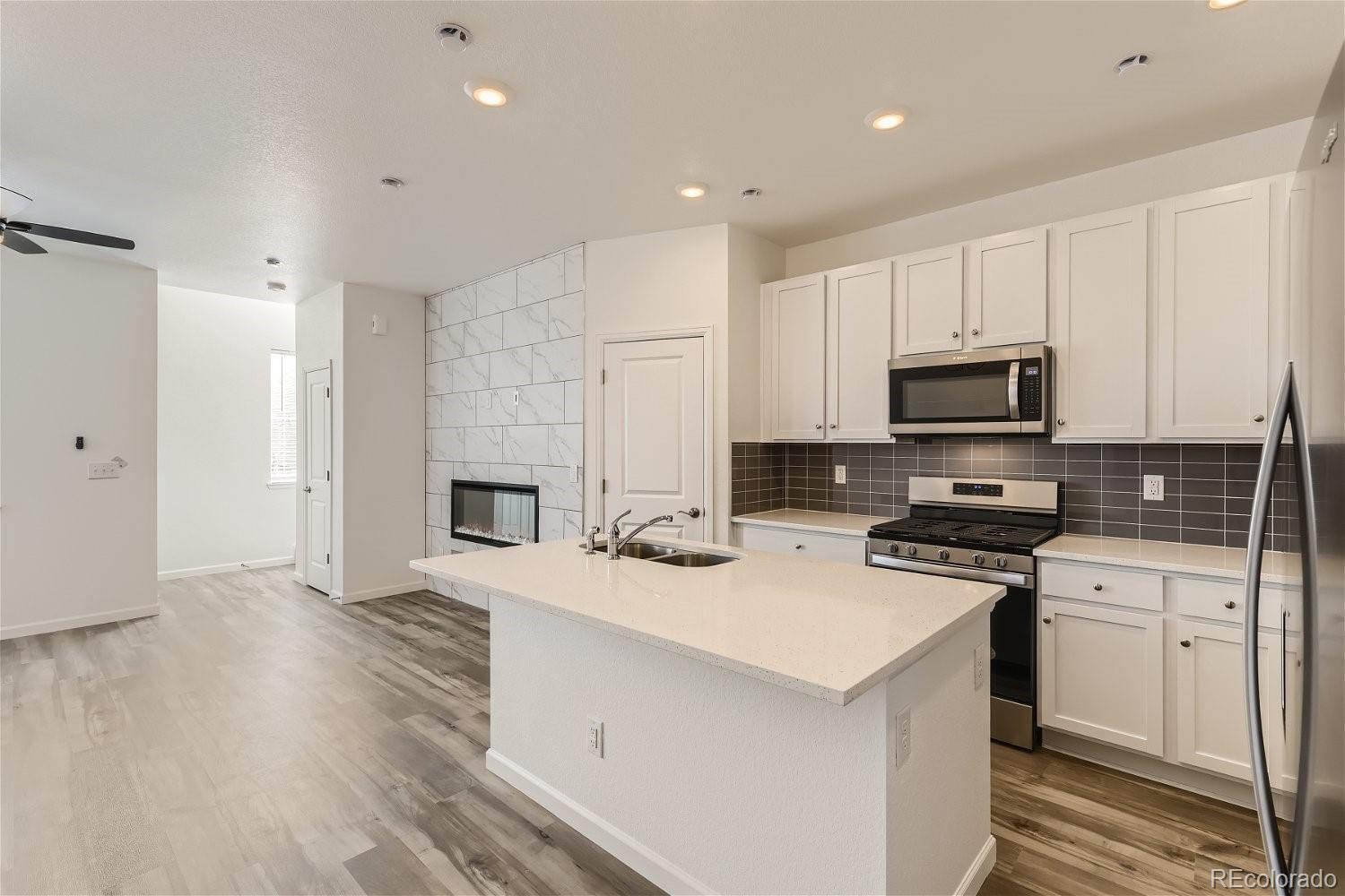 12659 Boggs Street Parker, CO 80134 - Photo 11 of 28 a kitchen with stainless steel appliances a stove top oven a sink a refrigerator white cabinets and wooden floor