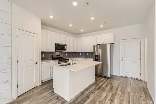 a kitchen with a refrigerator a stove top oven and white cabinets with wooden floor