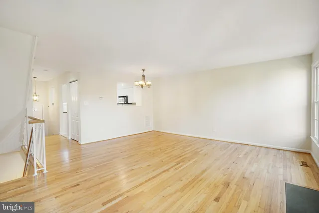 a view of empty room with wooden floor and kitchen