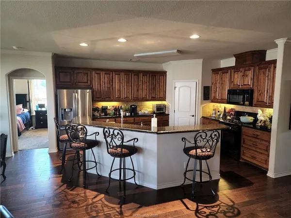 a kitchen with stainless steel appliances kitchen island granite countertop a stove a refrigerator a sink a dining table and chairs with wooden floor