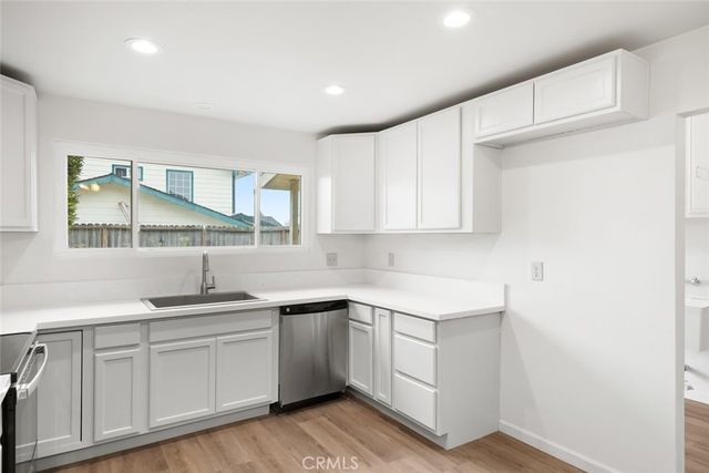 a kitchen with a sink dishwasher a stove and white cabinets with wooden floor