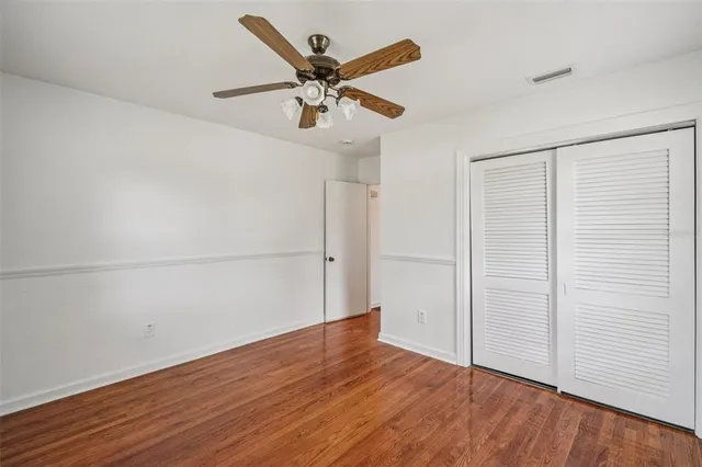 an empty room with wooden floor ceiling fan and windows