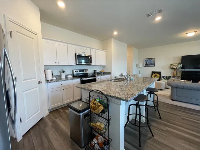 a open kitchen with stainless steel appliances granite countertop a stove a refrigerator a microwave a sink and white cabinets with wooden floor