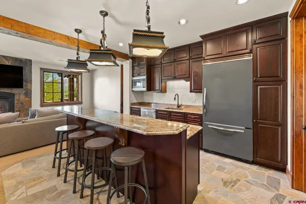 a kitchen with stainless steel appliances granite countertop a refrigerator a sink a stove and chairs